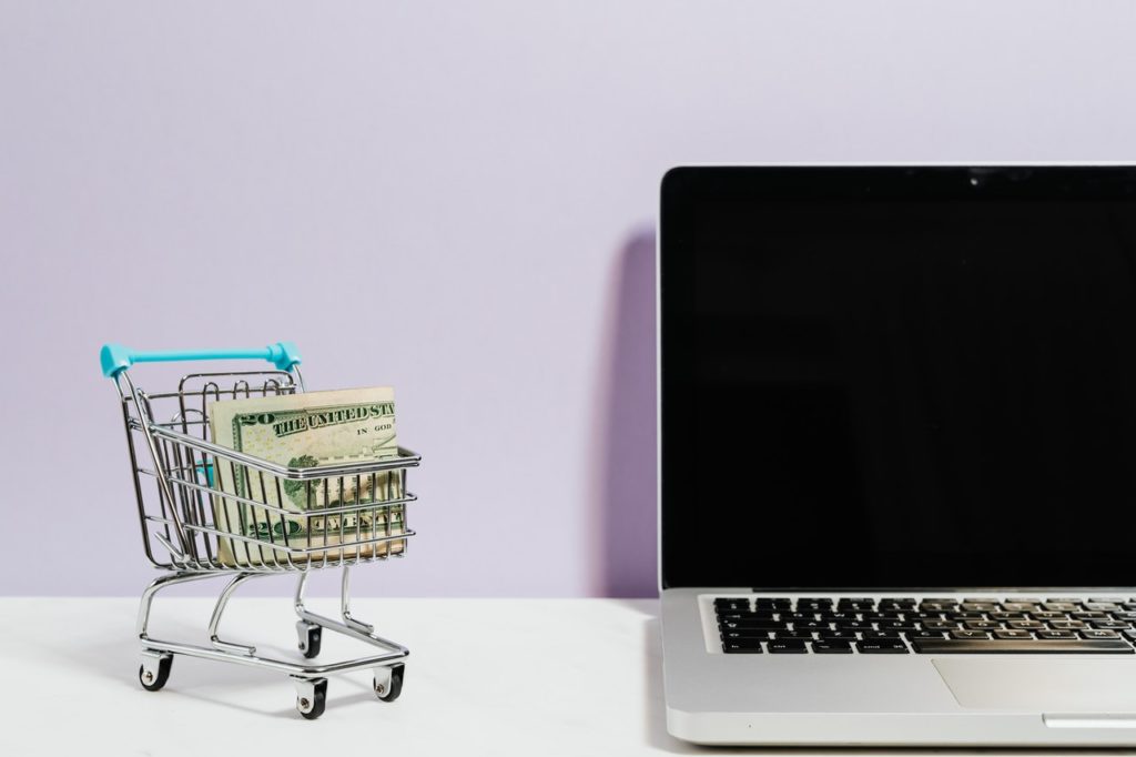 Shopping cart with money next to laptop