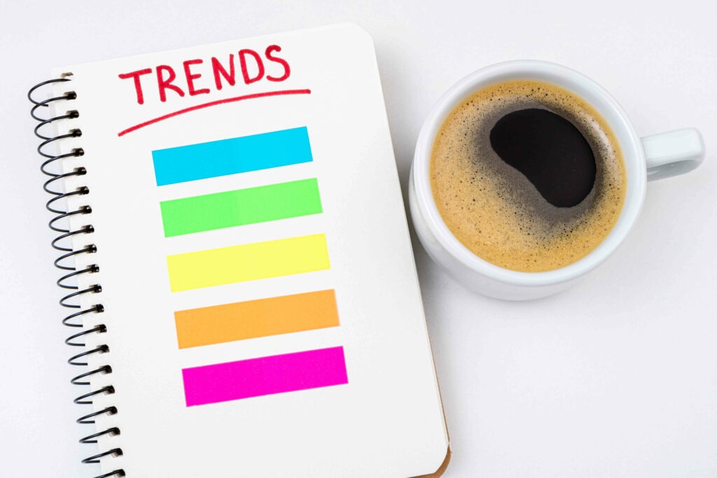 2023 trends business concept. Notebook with trends list, coffee cup on white background. Popular, relevant topics, trends, fashionable, fashion concept. Top view